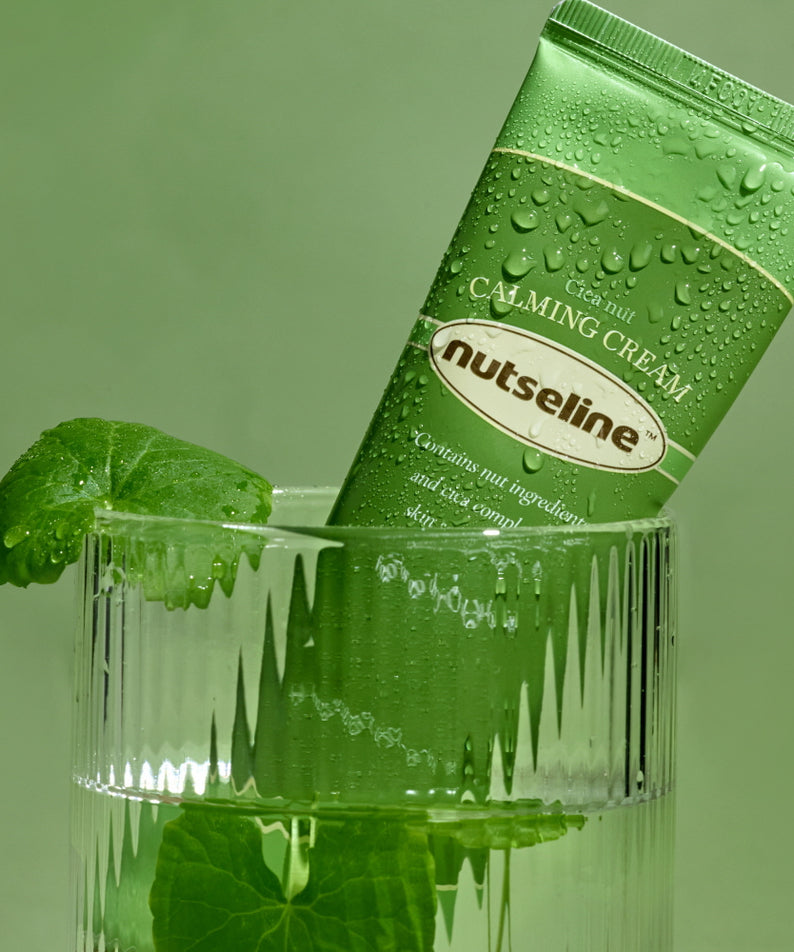Crème apaisante NUTSELINE Cica Nut Calming Cream 60ml dans un verre, mise en scène nature avec feuille verte, emballage vert élégant.