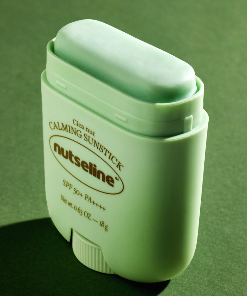 Stick solaire NUTSELINE Cica Nut Calming Sun Stick 18g avec protection SPF50+ sur fond vert élégant.