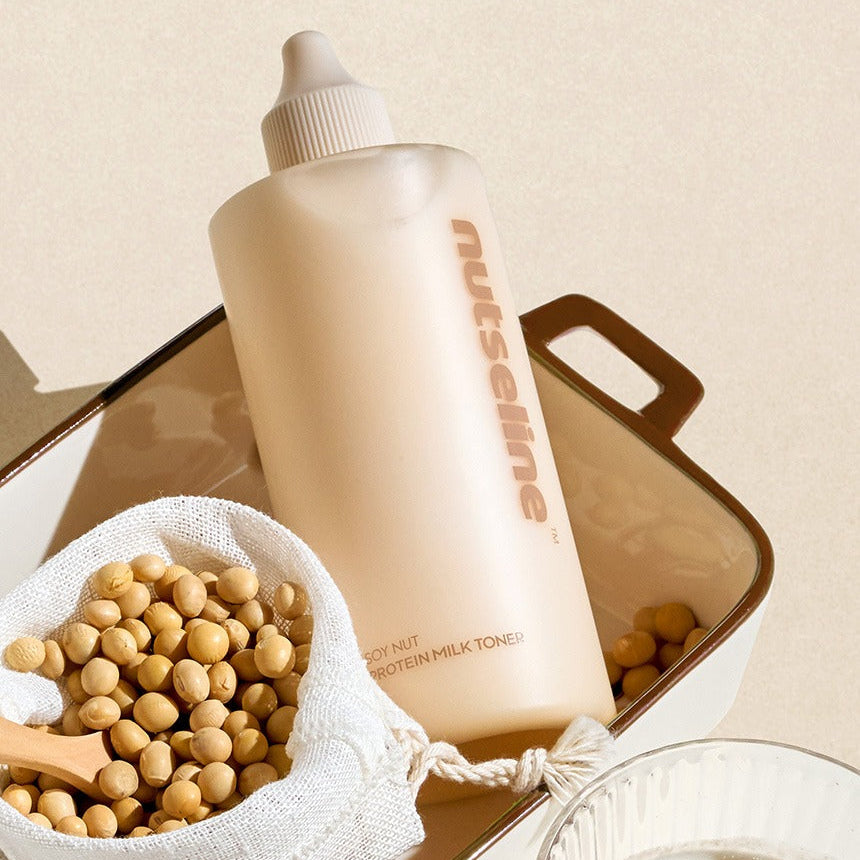 NUTSELINE Soy Nut Protein Milk Toner 300ml : flacon beige sur fond neutre avec sachet de soja et accessoires visuels.