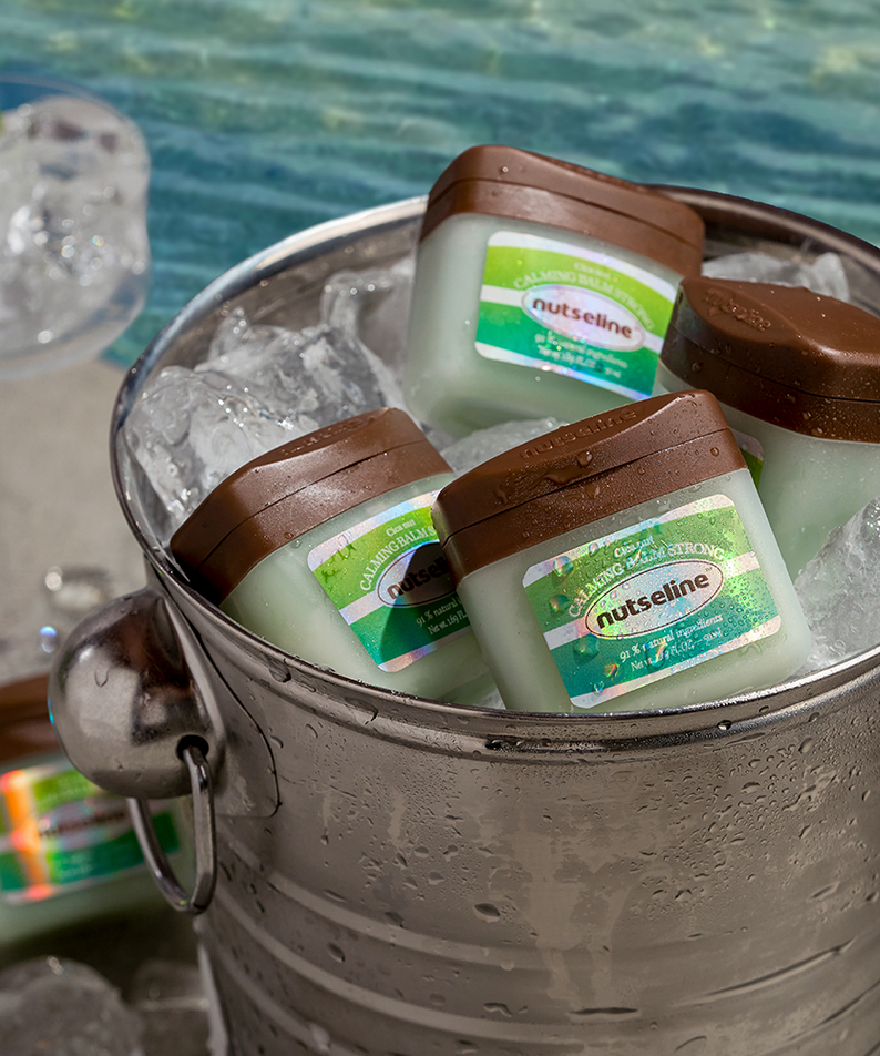 NUTSELINE Cica Nut Calming Balm Strong 50ml, crème apaisante pour peau, pots refroidissants dans un seau en bord de piscine.