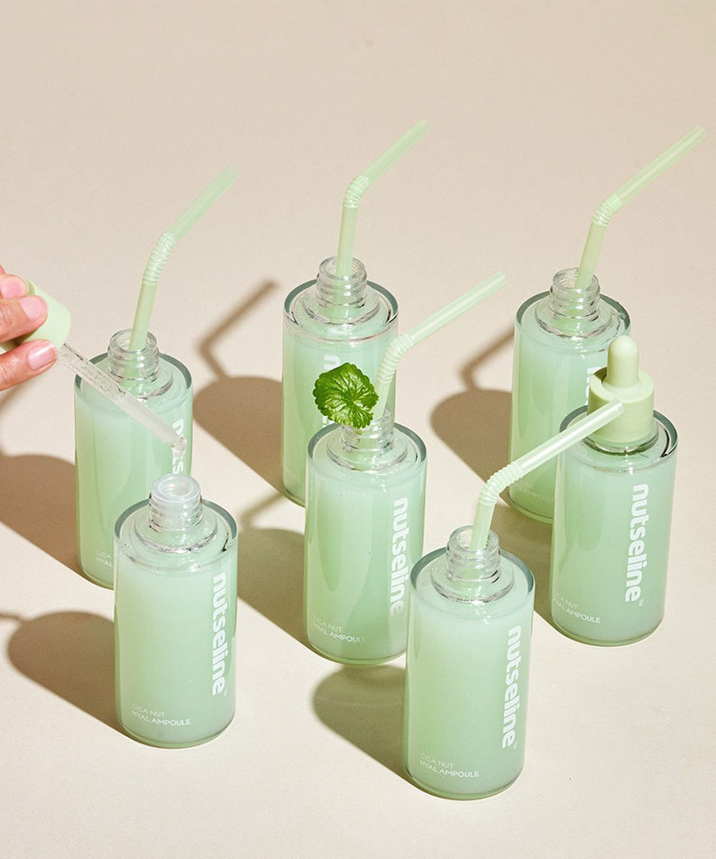 Flacons de 90ml de NUTSELINE Cica Nut Hyal Ampoule avec des pipettes et pailles sur une surface beige.