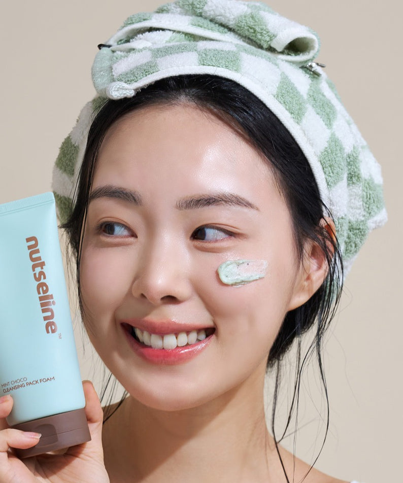 Femme souriante utilisant le NUTSELINE Mint Chocolate Cleansing Pack Foam 130g avec serviette à carreaux sur la tête.