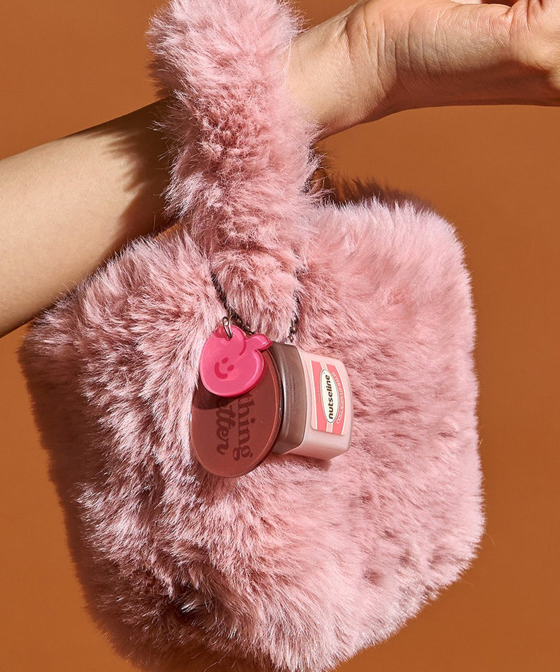 Lèvres douces et soyeuses avec le NUTSELINE Super Nut Collagen Keyring Lip Balm 11ml, accroché sur un sac à main en peluche rose foncé.