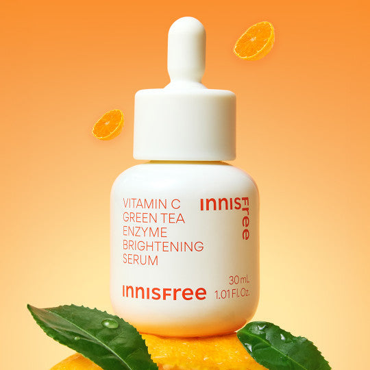 INNISFREE Vitamin C Green Tea Enzyme Brightening Serum, flacon sur fond orange avec feuilles de thé vert et agrumes