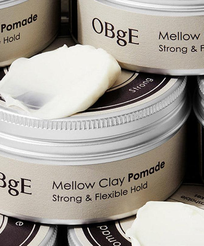 OBGE Mellow Clay Pomade 100g d’OBGE : pots de pomade à l’arrière-plan, vue rapprochée en salle de soins capillaires.