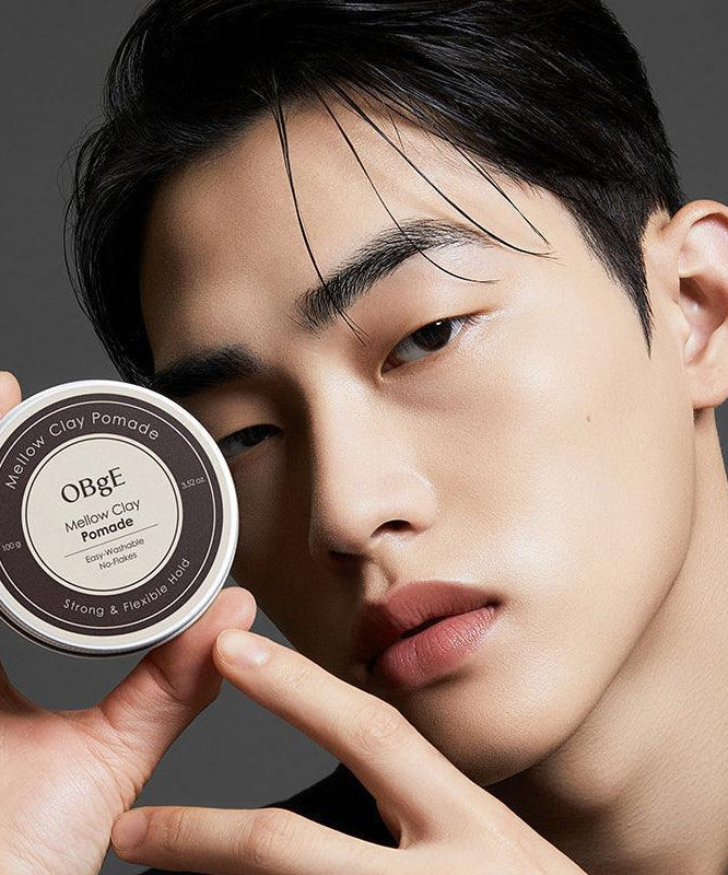 OBGE Mellow Clay Pomade 100g d’OBGE, homme tenant le pot sur fond gris, style coiffure naturel.