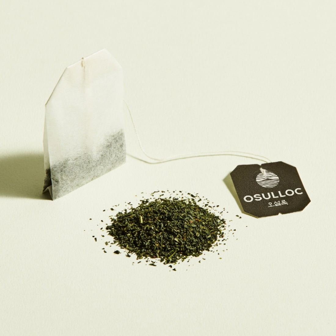OSULLOC Jeju Pure Green Tea 20 P : feuilles de thé vert en vrac avec sachet et logo, fond clair minimaliste.