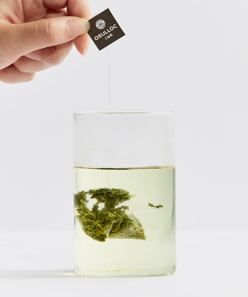 OSULLOC Sejack Green Tea 20 P : sachet vert infusé, marque OSULLOC, main tenant l’étiquette, fond clair, photo produit.