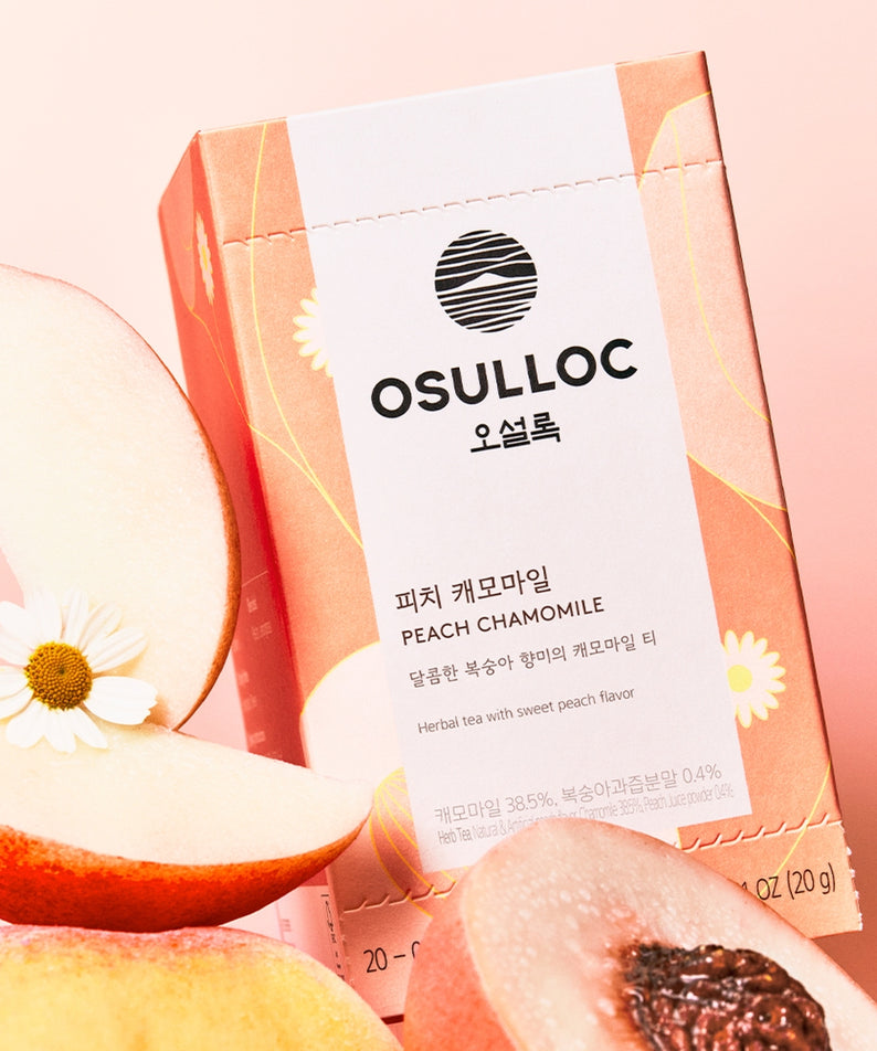 Boîte de thé OSULLOC Peach Chamomile 20 P, entourée de pêches et fleurs de camomille, en arrière-plan rose.