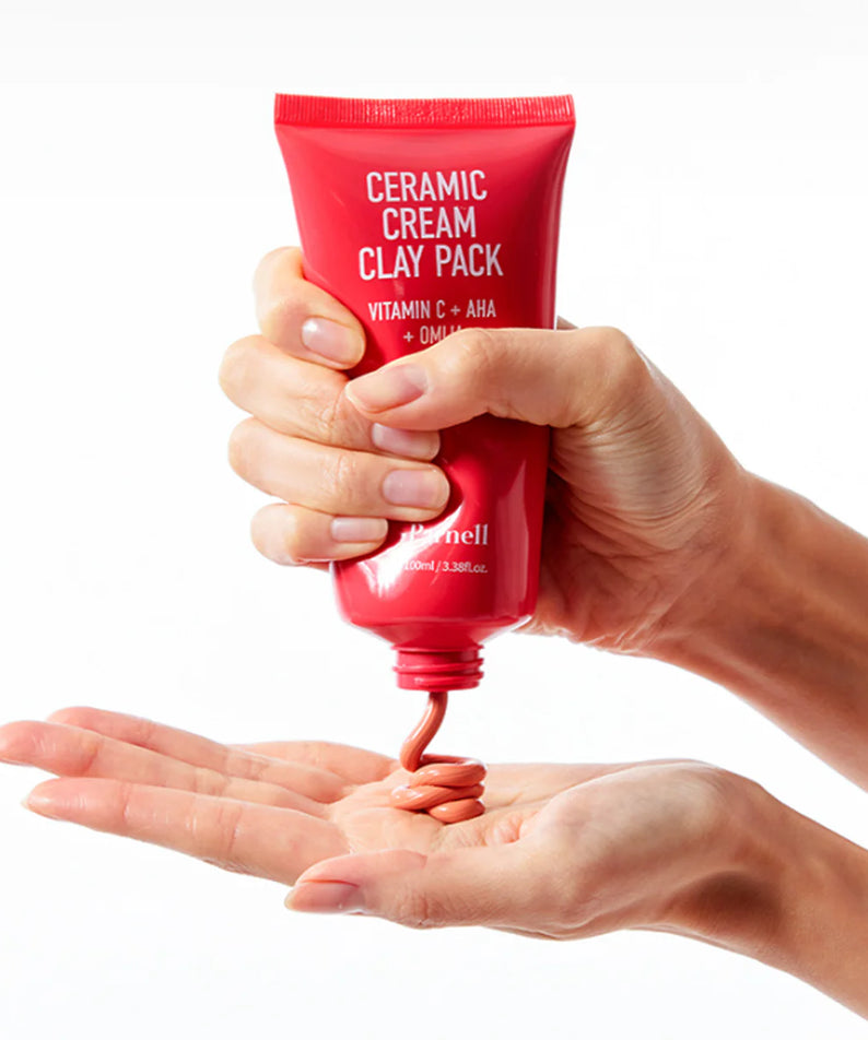 PARNELL  AHA Omija Ceramic Cream Clay Pack 100ml, tube rouge tenu dans les mains, fond blanc, crème argile AHA/Céramic