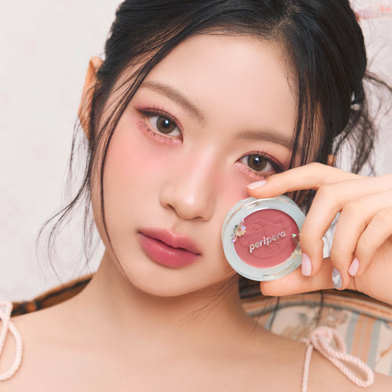 PERIPERA Pure Blushed Sunshine Cheek, produit cosmétique sur fond clair: maquillage rosé près des joues, main tenant le pot.