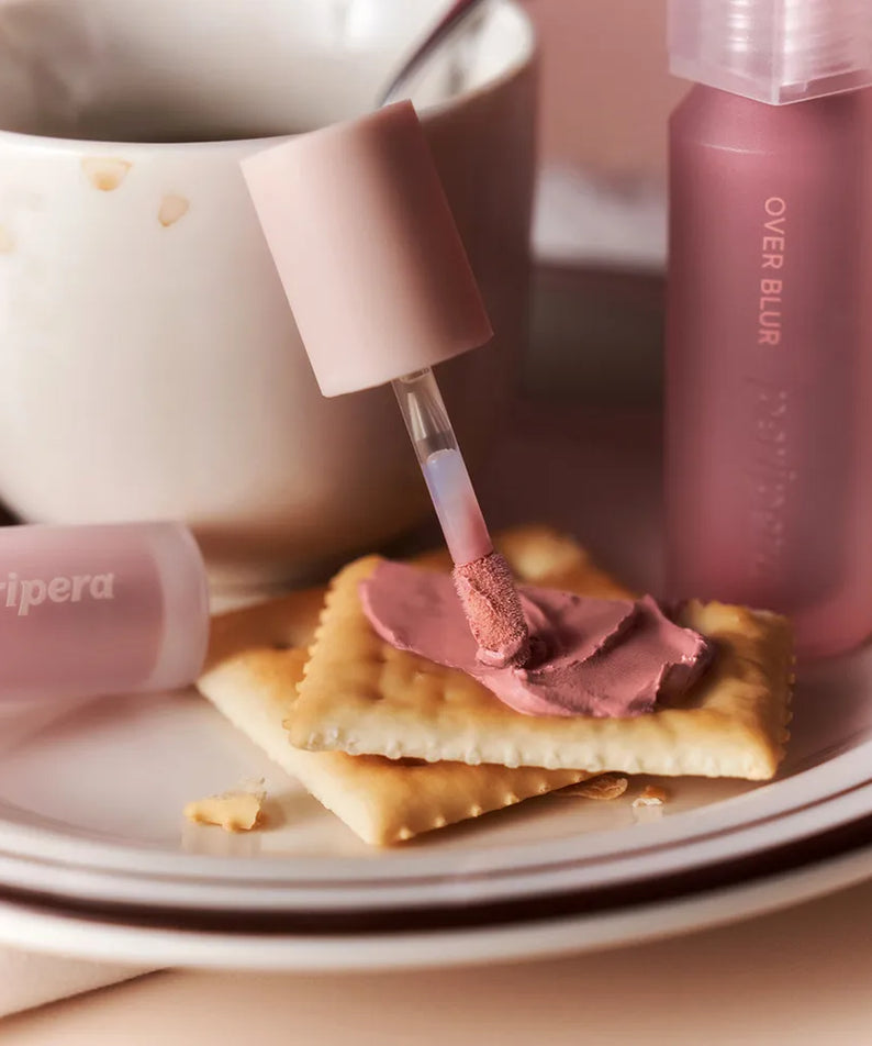 PERIPERA Over Blur Tint de la marque PERIPERA, flacons roses sur plateau crème, démo maquillage blur.