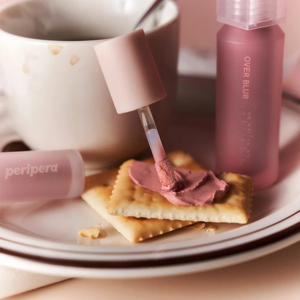 PERIPERA Over Blur Tint de la marque PERIPERA, flacons roses sur plateau crème, démo maquillage blur.
