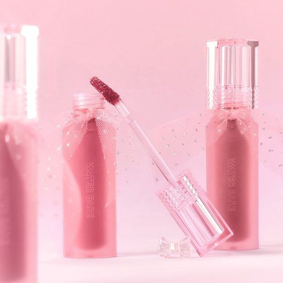 PERIPERA Water Bare Tint, maquillage lèvres rose en flacon et applicateur, fond pastel rose avec gouttelettes (Décris l'image).