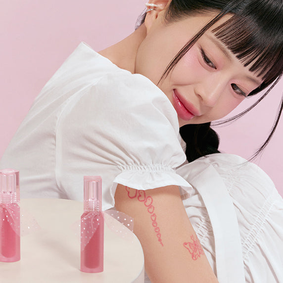 PERIPERA Water Bare Tint : maquillage nude rosé, femme aux lèvres brillantes, flacons roses sur fond rose