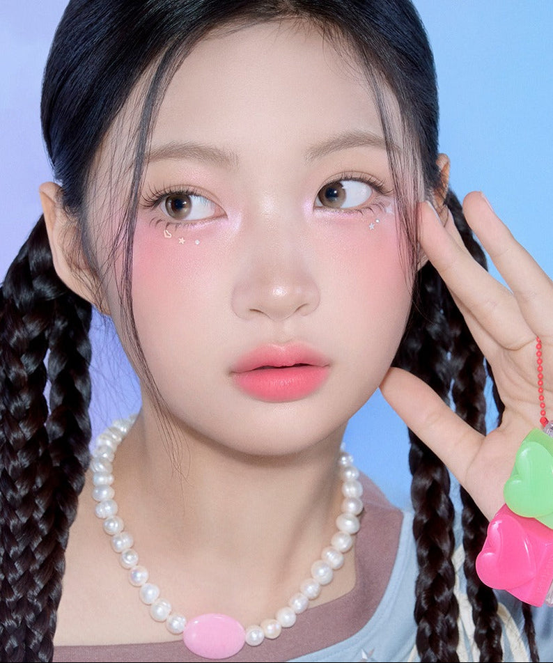 Jeune femme portant PERIPERA Talk Blush Keycap, son visage embellit par une touche de blush vibrant. Décor pastel et élégant.