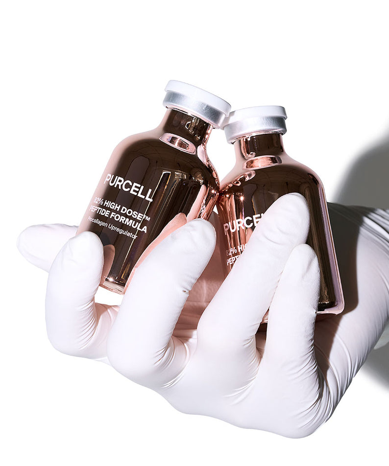 PURCELL 82% High Dose™ Peptide Formula 30mL, flacons tenus par des gants médicaux en contexte de soin.