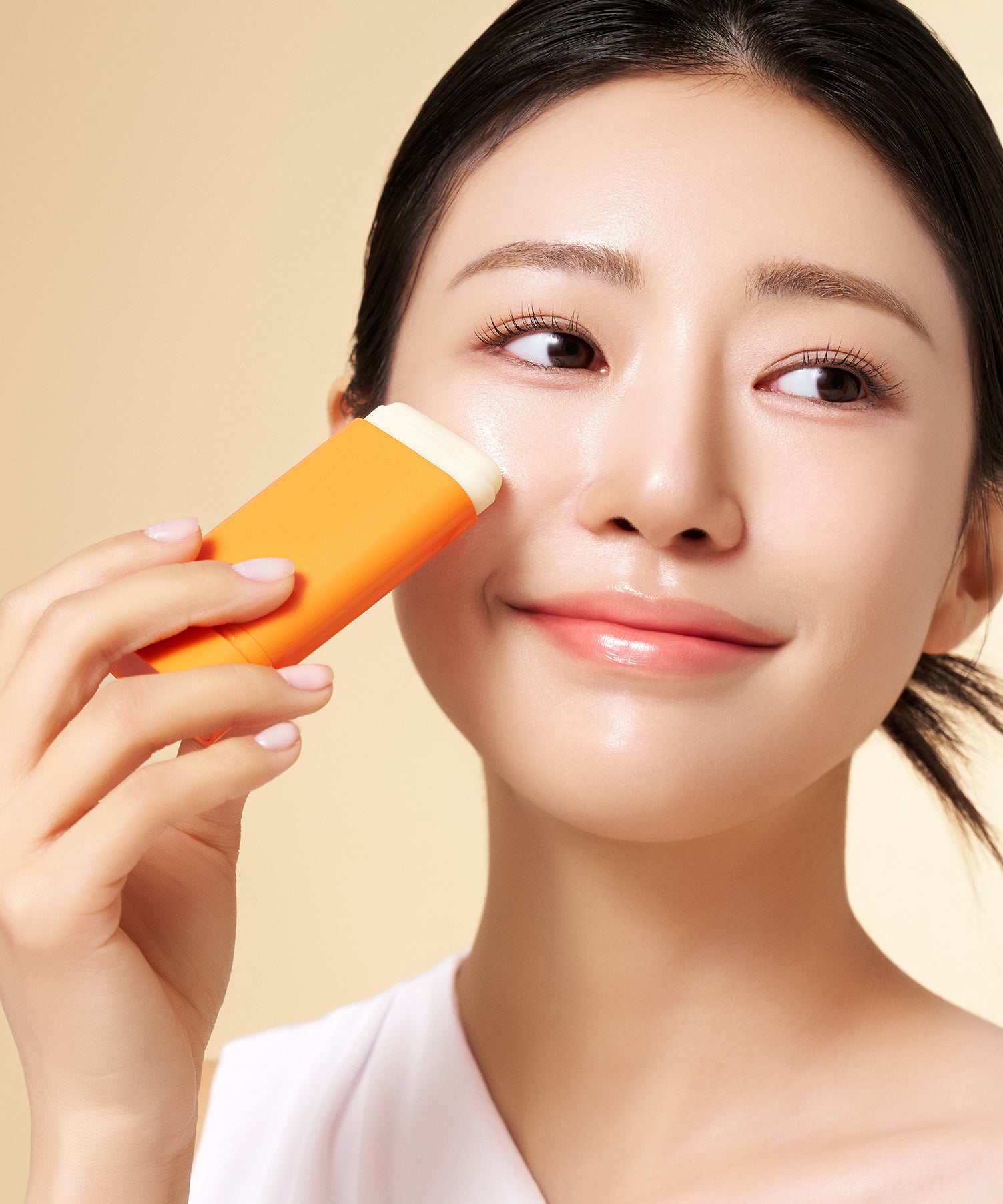 PURITO Daily Soft Touch Sun Stick SPF50+PA++++ : femme applique un stick solaire orange, fond beige, peau lumineuse.