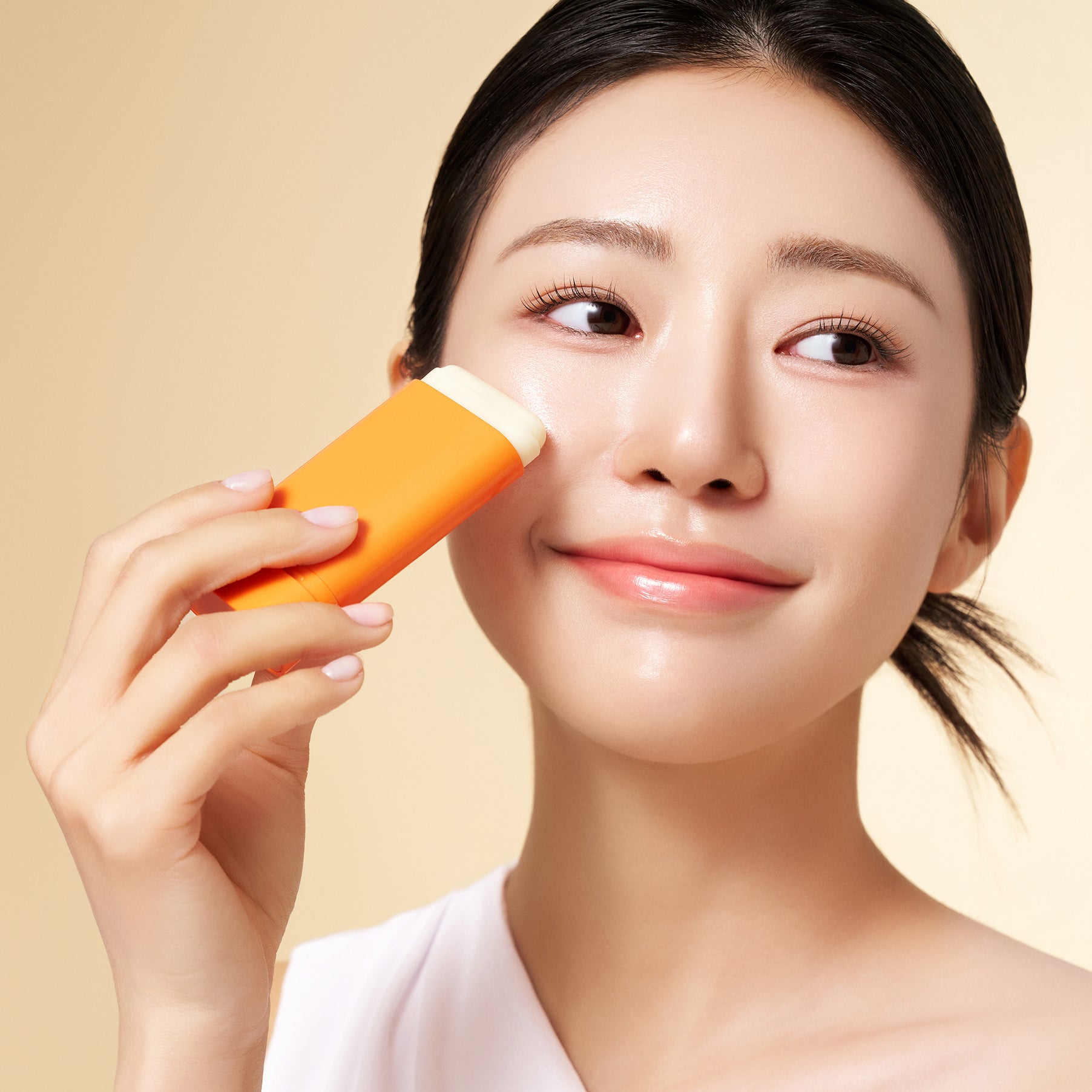 PURITO Daily Soft Touch Sun Stick SPF50+PA++++ : femme applique un stick solaire orange, fond beige, peau lumineuse.