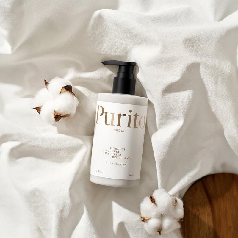 PURITO Luminous Moisture Shea Butter Body Lotion 300ml, flacon Purito sur tissu blanc avec coton, ambiance spa.