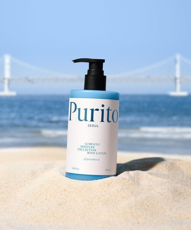 Lotion corporel hydratante PURITO Luminous Moisture Shea Butter Body Lotion 300ml sur une plage ensoleillée avec pont en arrière-plan.