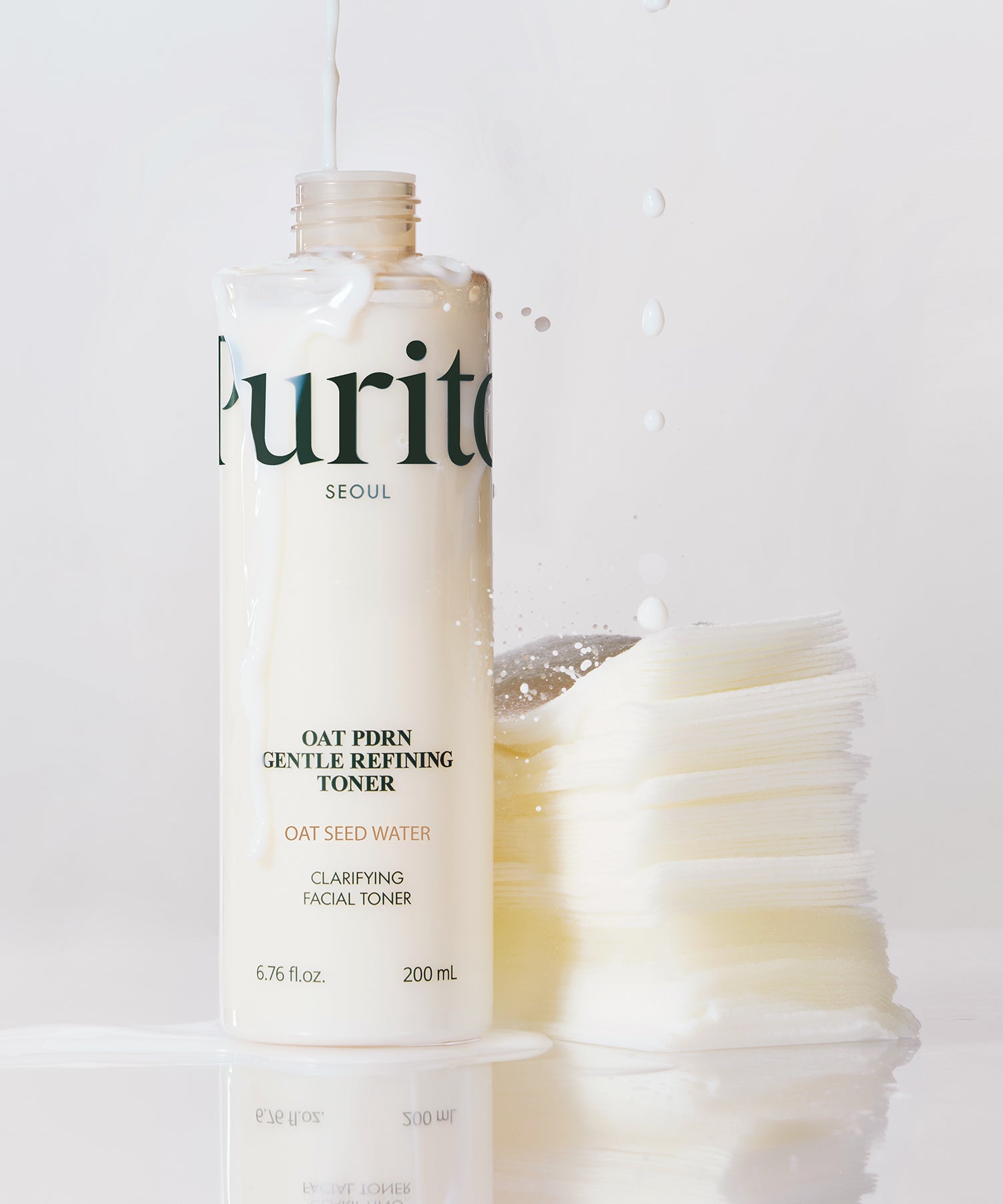 Bouteille de 200 ml du PURITO Oat PDRN Gentle Refining Toner avec eau d'avoine, posée debout avec des coton démaquillants. Parfaite pour clarifier la peau.