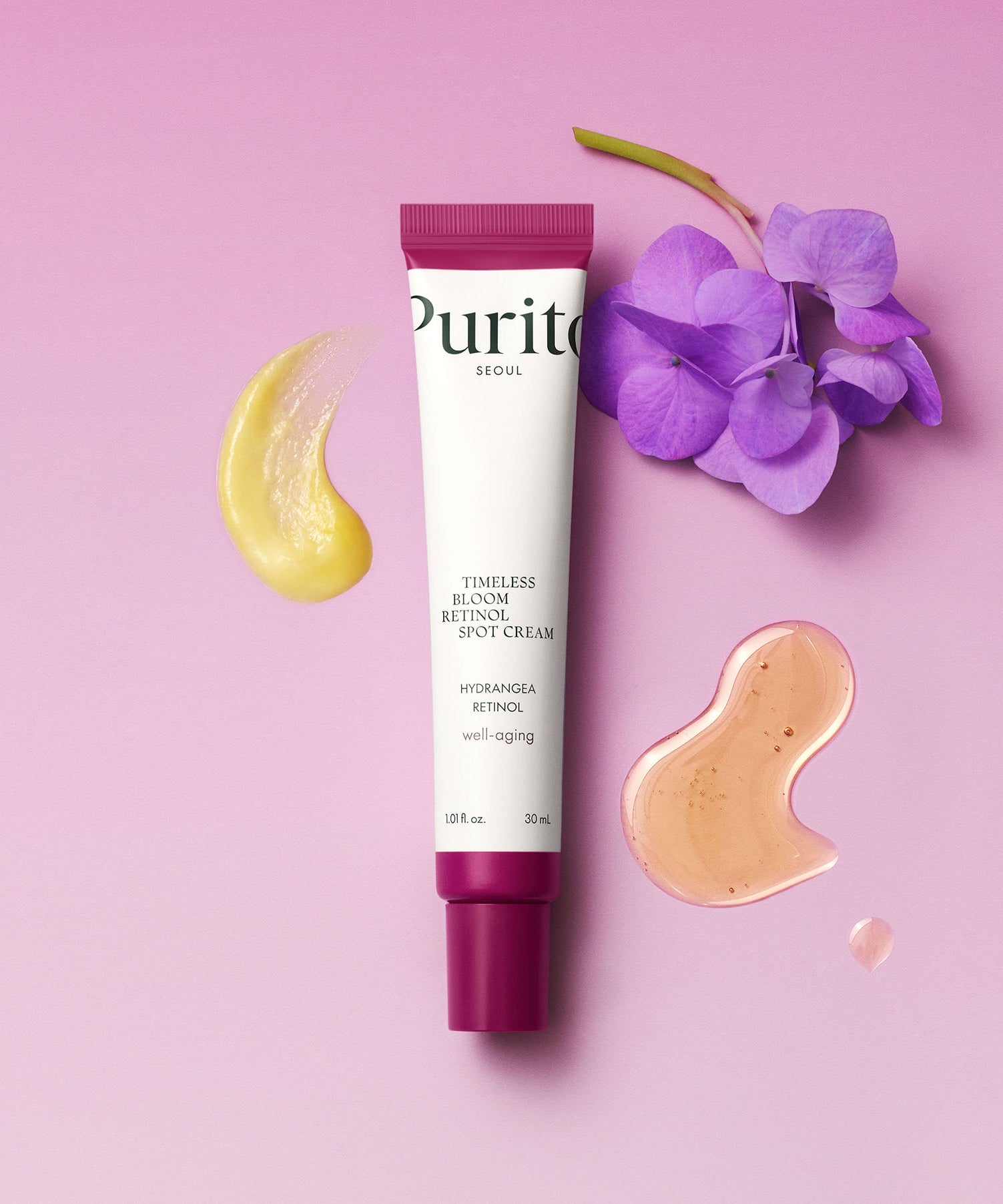 Tube de PURITO Timeless Bloom Retinol Spot Cream 30ml sur fond rose avec fleurs violettes et texture crème.