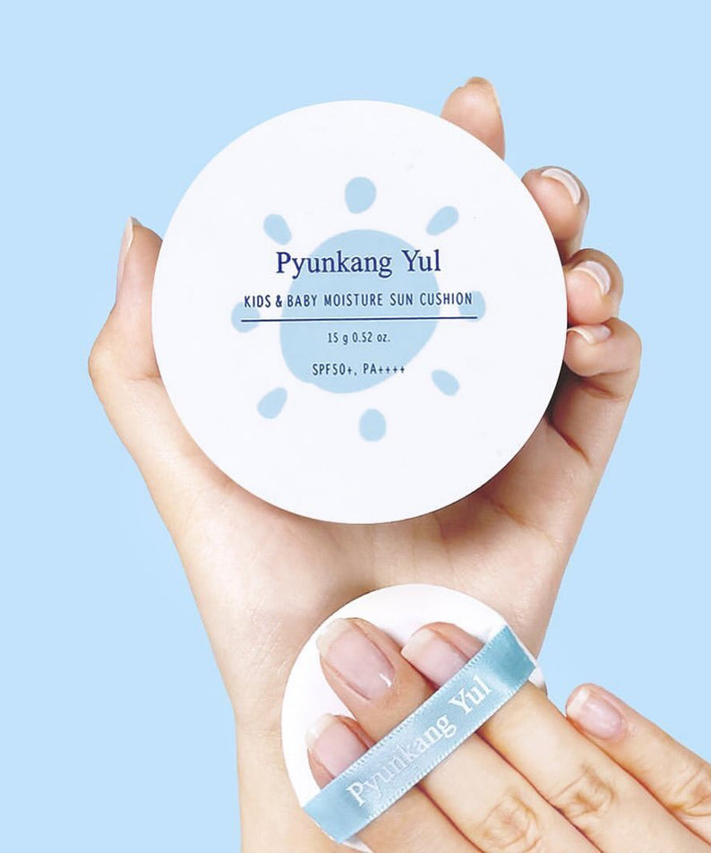 PYUNGKANG YUL Kids & Baby Moisture Sun Cushion SPF50+ PA++++ 15g, boîte blanche tenue par des mains sur fond bleu.