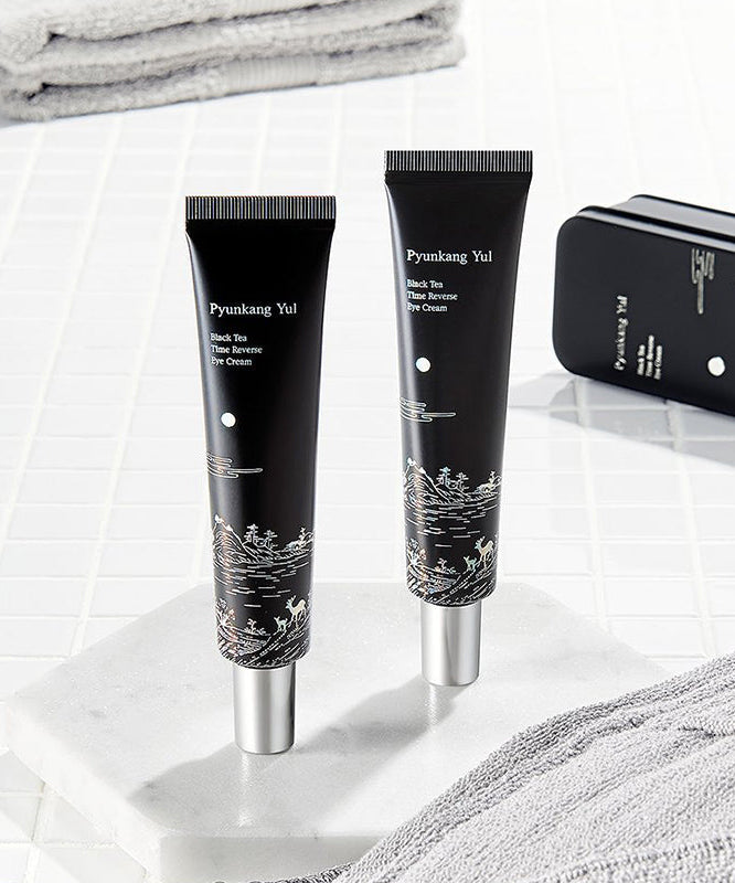 PYUNKANG YUL Black Tea Time Reverse Eye Cream 25ml : tubes noirs sur fond blanc, serviettes et décor spa.