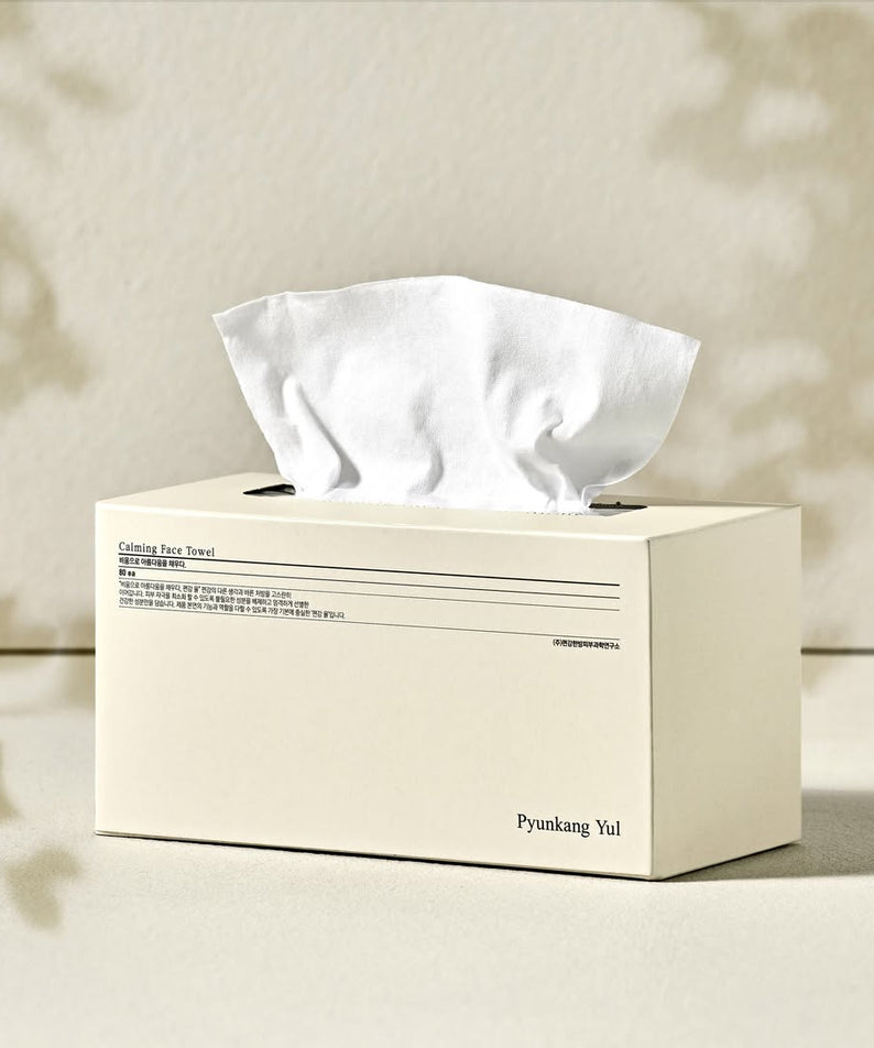 Boîte de PYUNKANG YUL Calming Face Towels 80 Pieces sur une table, avec serviettes blanches sortant du dessus, fond beige.