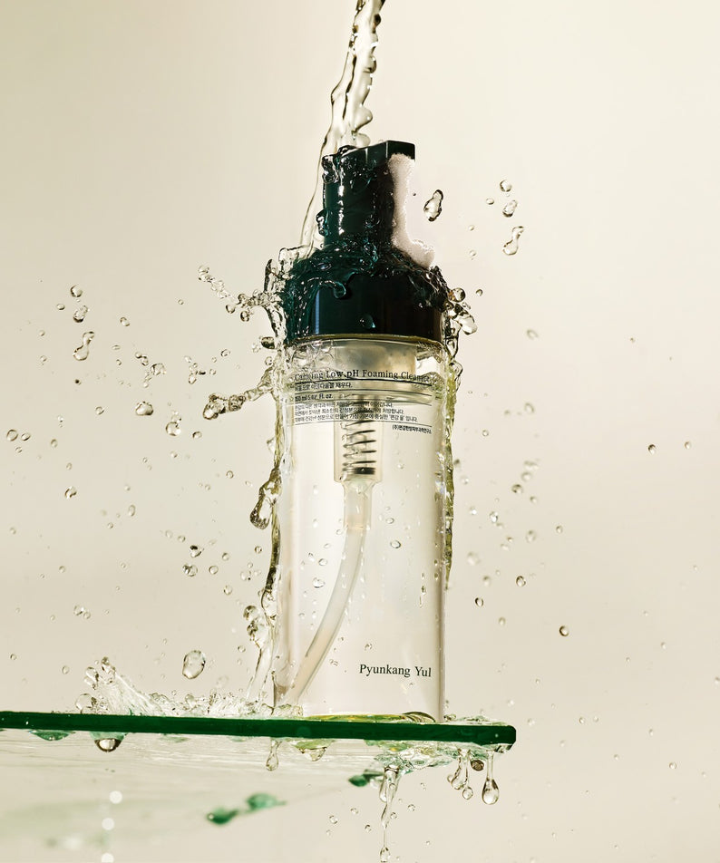 Flacon de 150ml du PYUNKANG YUL Calming Low pH Foaming Cleanser sous un jet d'eau, conçu pour le nettoyage apaisant de la peau.