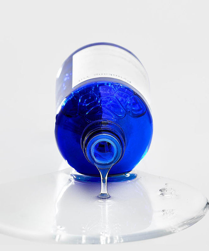 Flacon bleu de PYUNKANG YUL Moisture Ampoule 100ml, sérum hydratant en train de couler sur une surface blanche, soin de la peau.