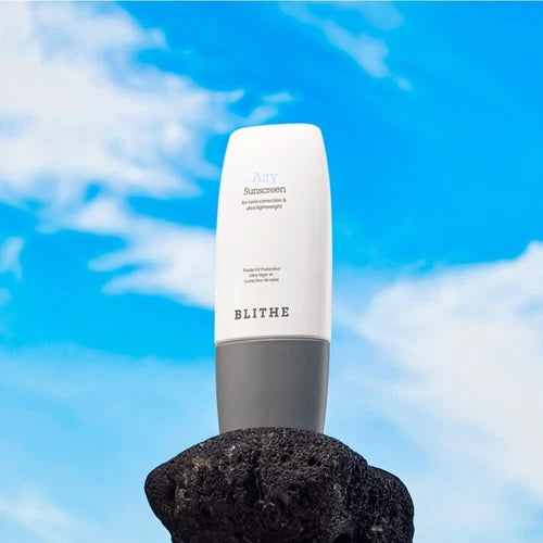 BLITHE Airy Sunscreen 50ml de la marque BLITHE, flacon blanc sur une éponge noire, ciel bleu estival
