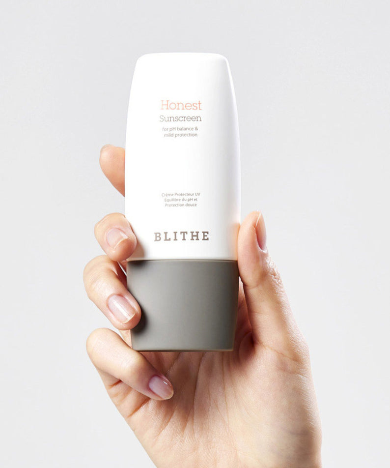 Main tenant BLITHE Honest Sunscreen 50ml, crème solaire blanche, fond clair minimaliste, marque BLITHE visible.