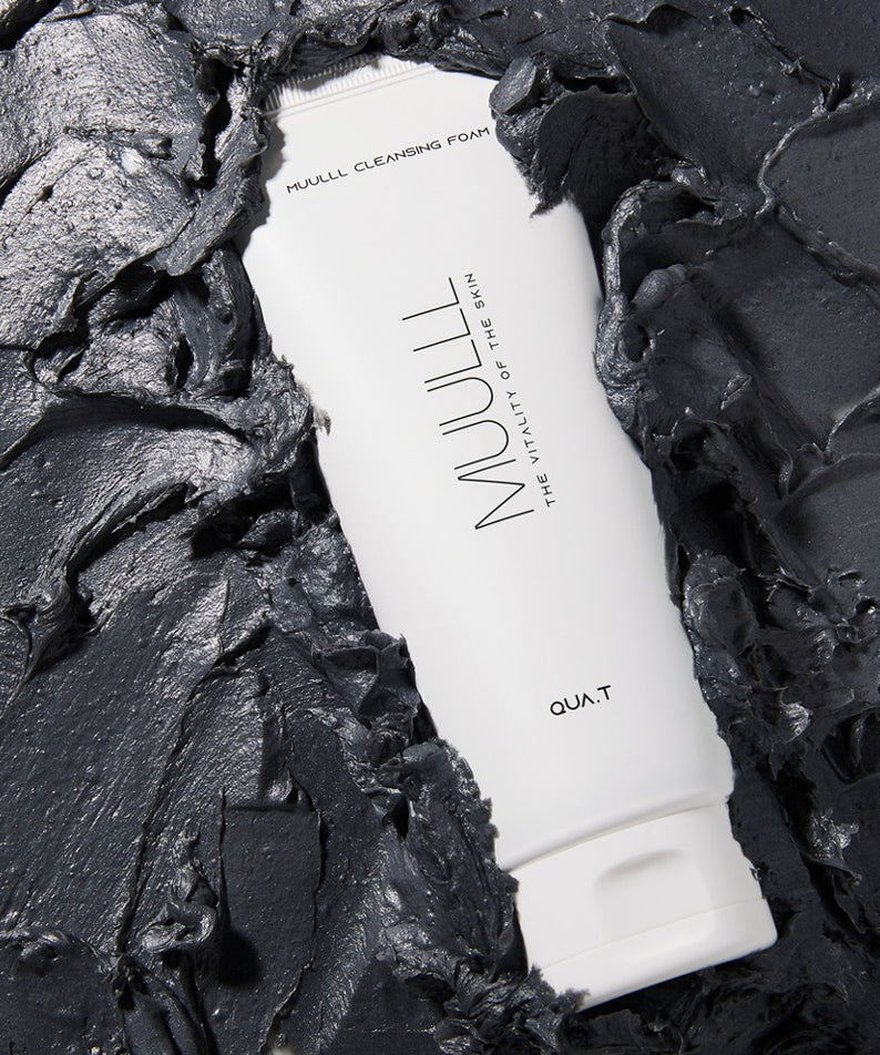 QUA-T Cleansing foam 150g de QUA.T, tube blanc sur fond noir texturé, mise en scène produit.