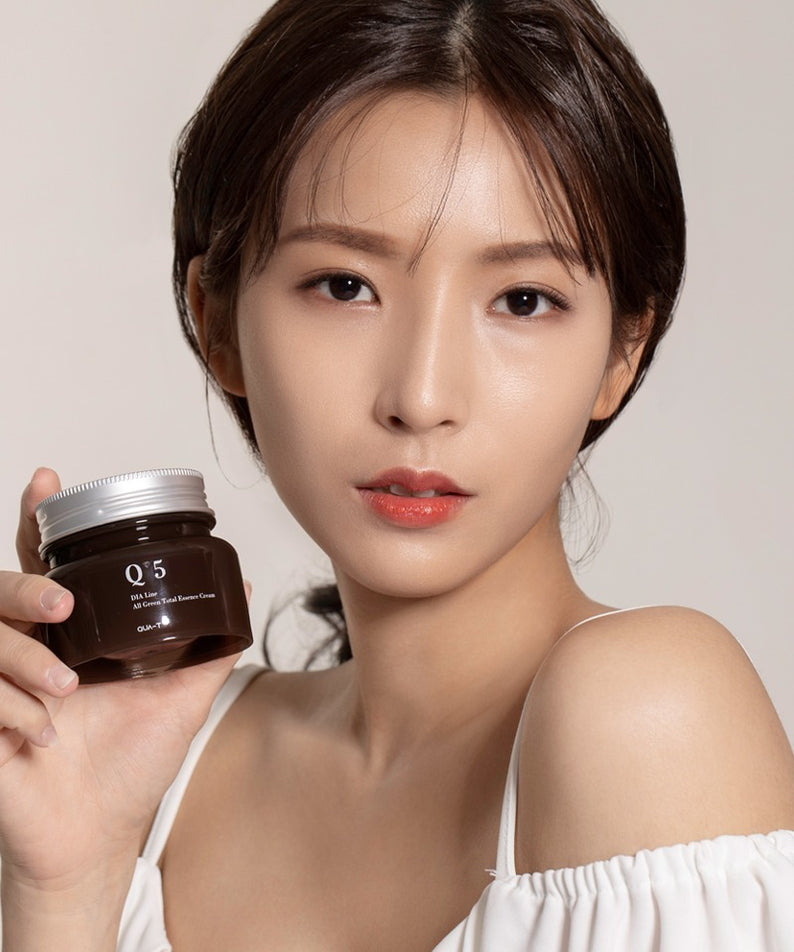 Portrait produit QUA-T Dia All Green Total Essence Cream 100ml de QUA-T, pot vert tenu par une femme sur fond clair.