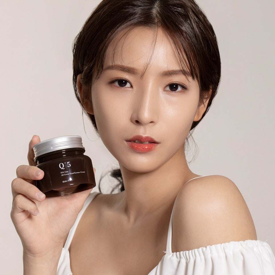 Portrait produit QUA-T Dia All Green Total Essence Cream 100ml de QUA-T, pot vert tenu par une femme sur fond clair.
