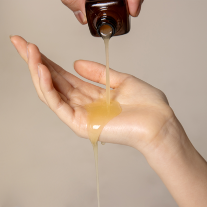 QUA-T Dia Peptide Jojoba Facial Serum 30ml QUA-T, serum doré coulant sur la main, contexte soins visage
