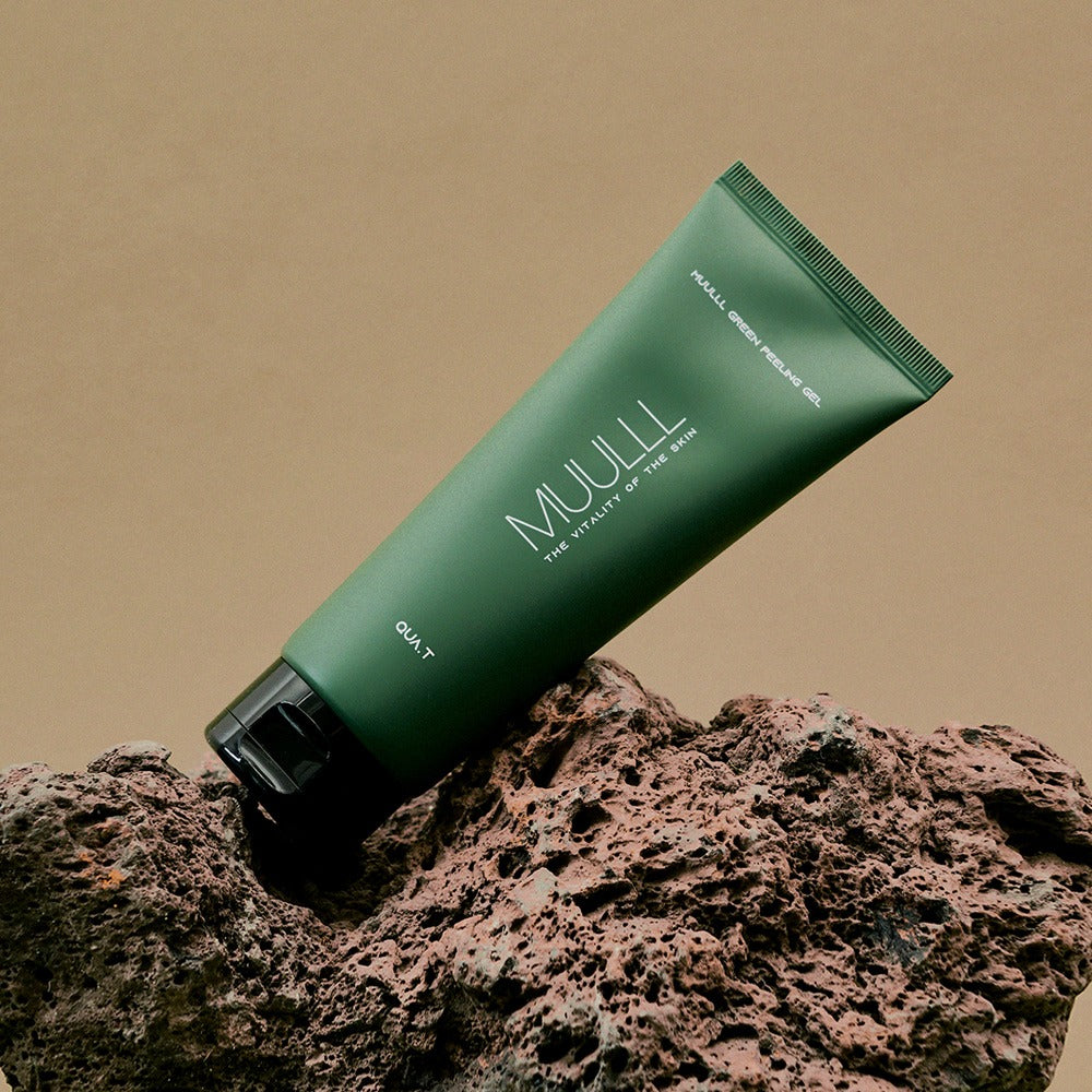 QUA-T Green Peeling Gel 150ml de la marque QUA-T, tube vert sur fond sable et roches, photo produit en studio.
