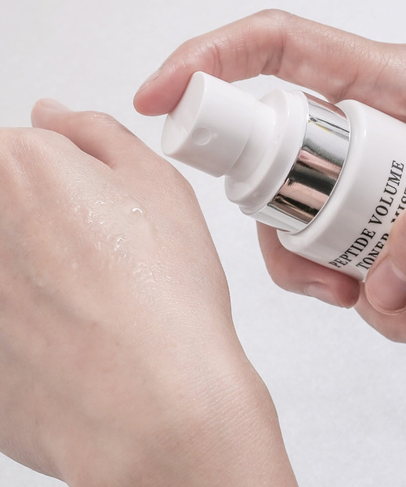 R828 Peptide Volume Toner Mist en main, pulvérisé sur la peau, image produit sur fond clair, soin visage.
