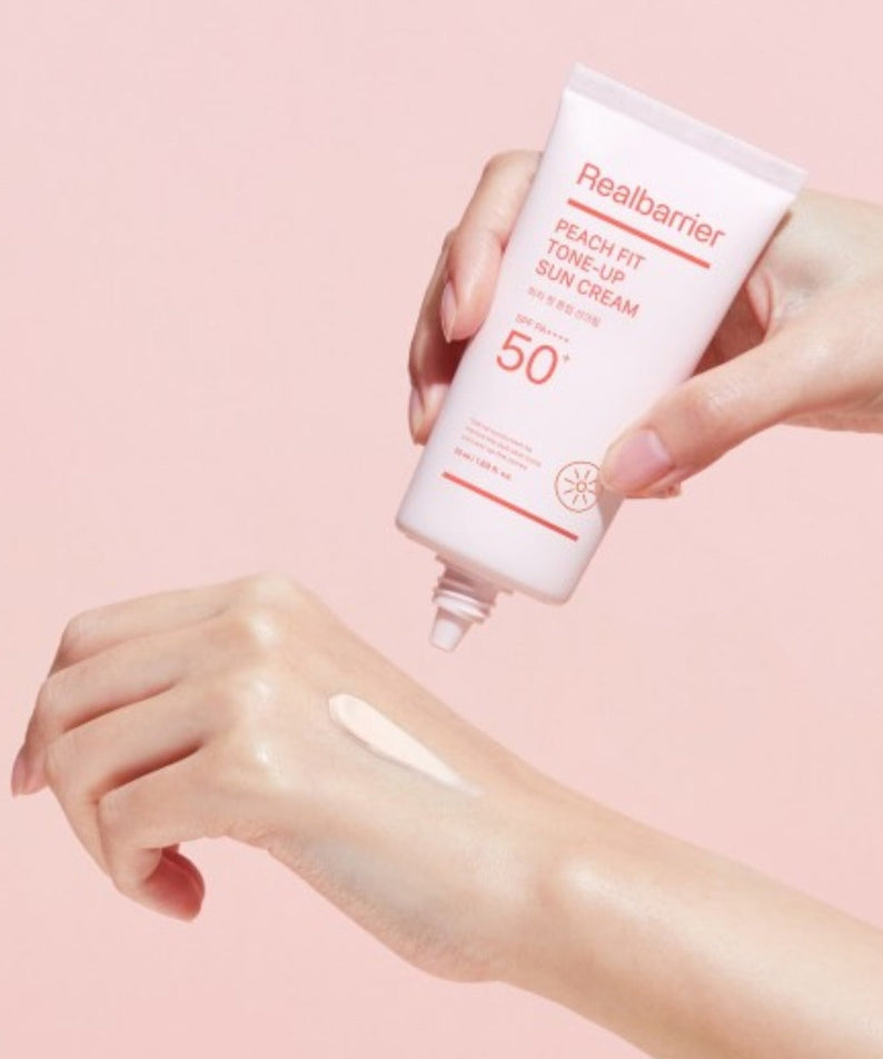 REAL BARRIER Peach Fit Tone-Up Sun Cream 50ml, crème solaire en tube, mains appliquant sur peau, fond rose, marque Real Barrier