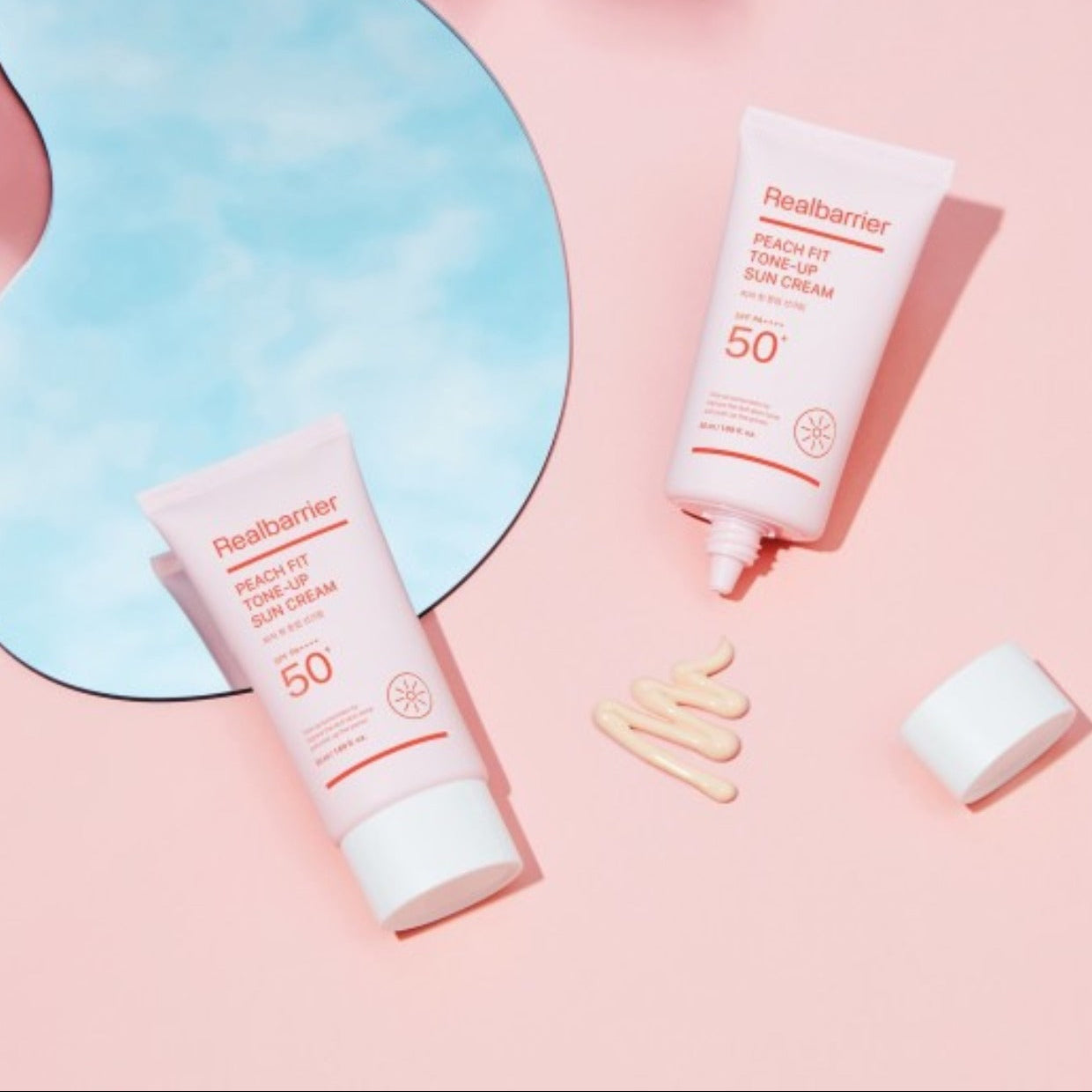 REAL BARRIER Peach Fit Tone-Up Sun Cream 50ml de marque Realbarrier, tubes solaires sur fond rose pastel, contexte beauté.