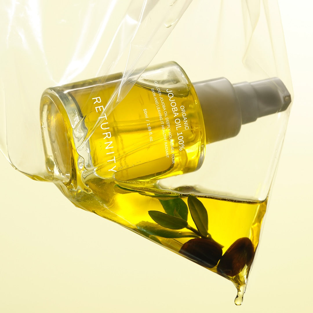 RETURNITY Organic Jojoba Oil 100% 50ml, flacon jaune et huile versée sur fond clair, avec feuilles de jojoba.