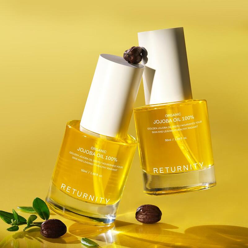 RETURNITY Organic Jojoba Oil 100% 50ml, flacons d’huile bio sur fond jaune ensoleillé, grains de café et feuilles vertes