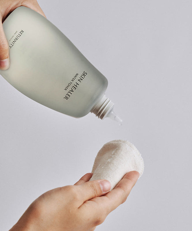 RETURNITY Skin Healer Water Toner 300ml de la marque RETURNITY, mains appliquant le toner sur un coton, fond clair