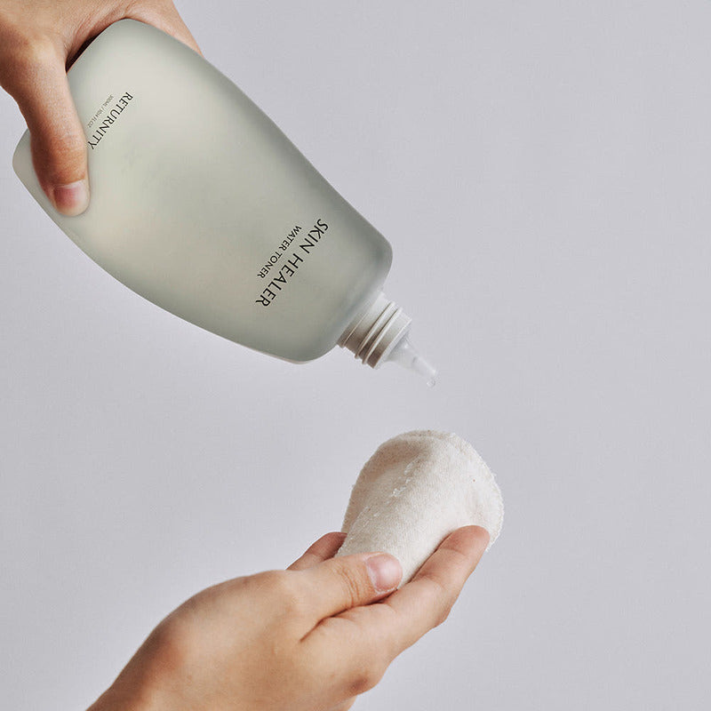 RETURNITY Skin Healer Water Toner 300ml de la marque RETURNITY, mains appliquant le toner sur un coton, fond clair