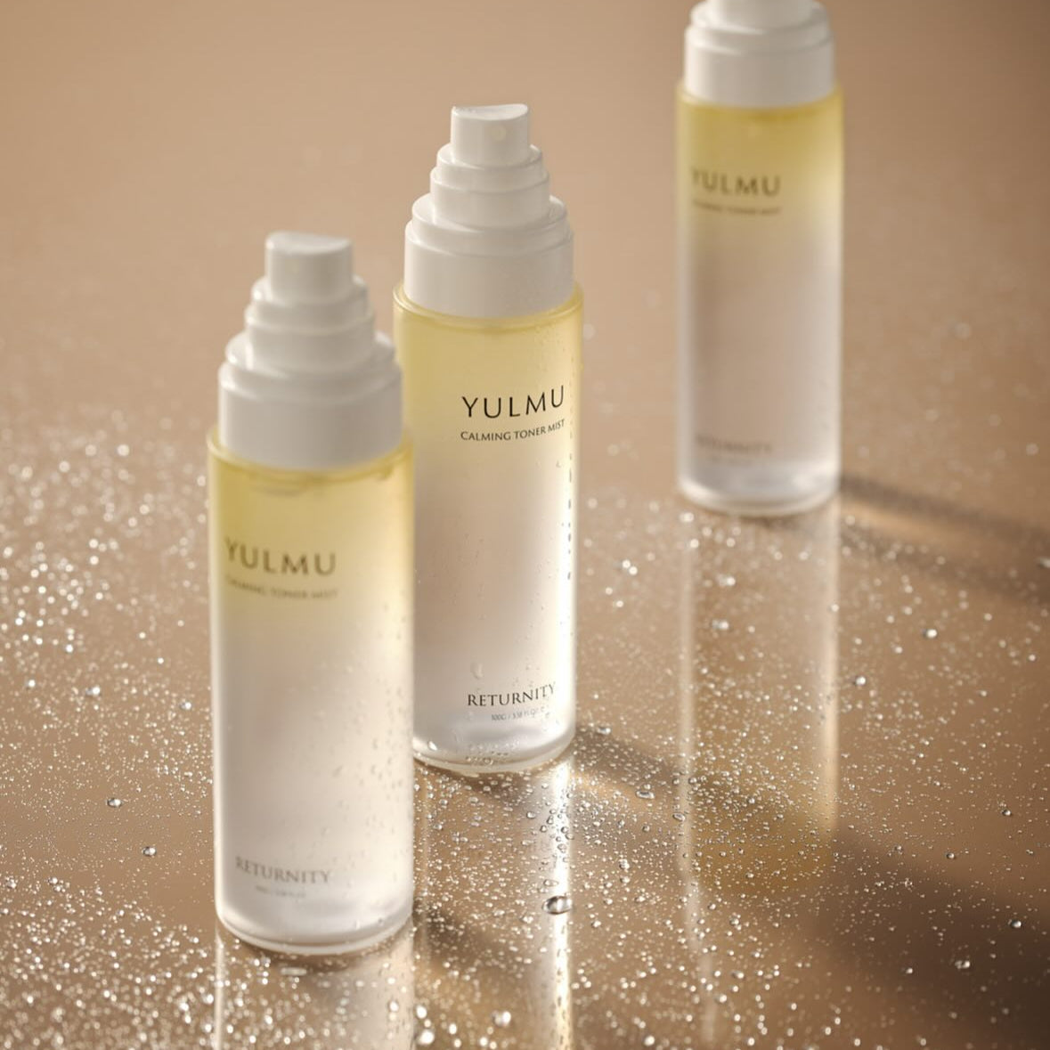 RETURNITY Yulmu Calming Toner Mist 100ml, bouteilles sur fond beige avec brume/particules, marque RETURNITY visible