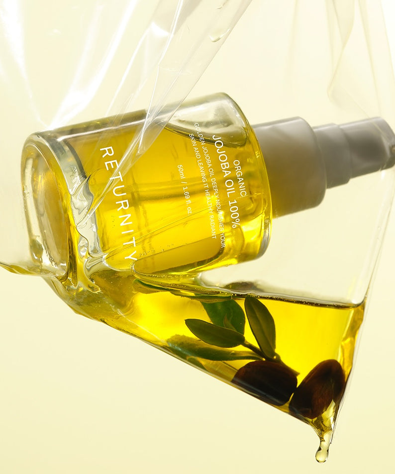 Flacon de 50ml d'huile de jojoba biologique RETURNITY Organic Jojoba Oil 100% avec bouchon doseur, posé sur fond jaune clair.