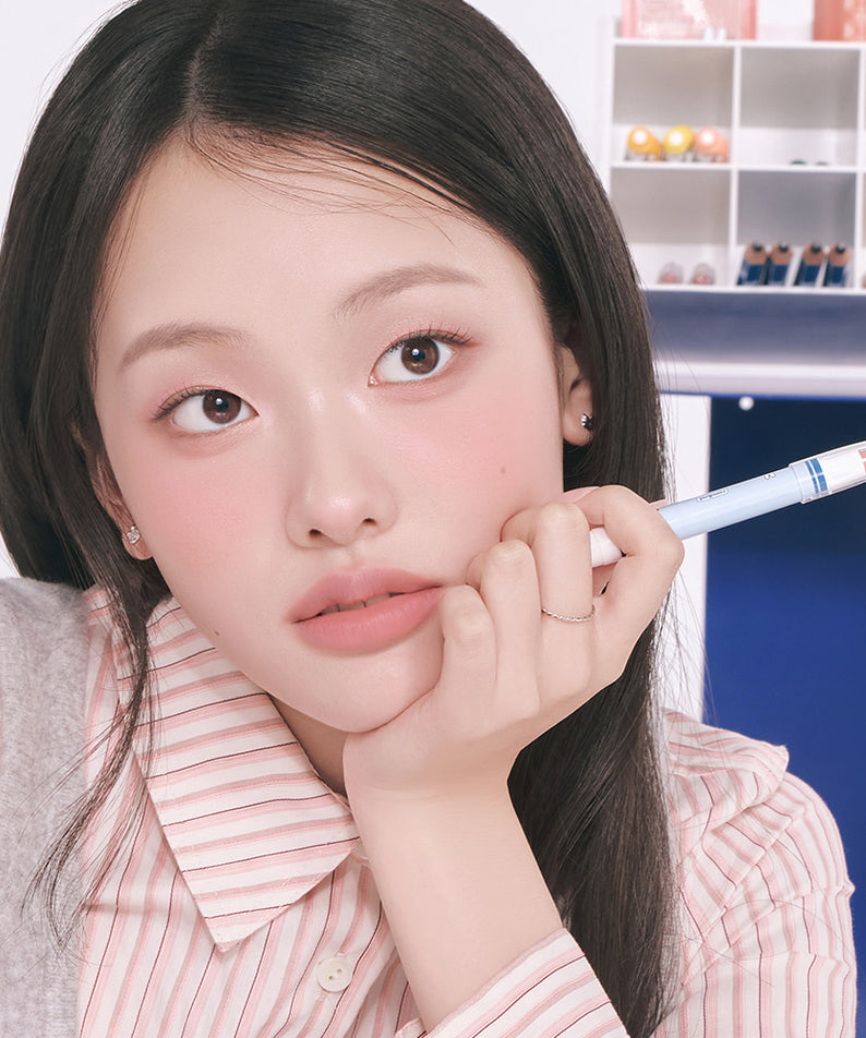 ROMAND  Blurpy Lip Crayon, maquillage lèvres : la femme tient le crayon près du visage, décor cosmétiques en arrière-plan