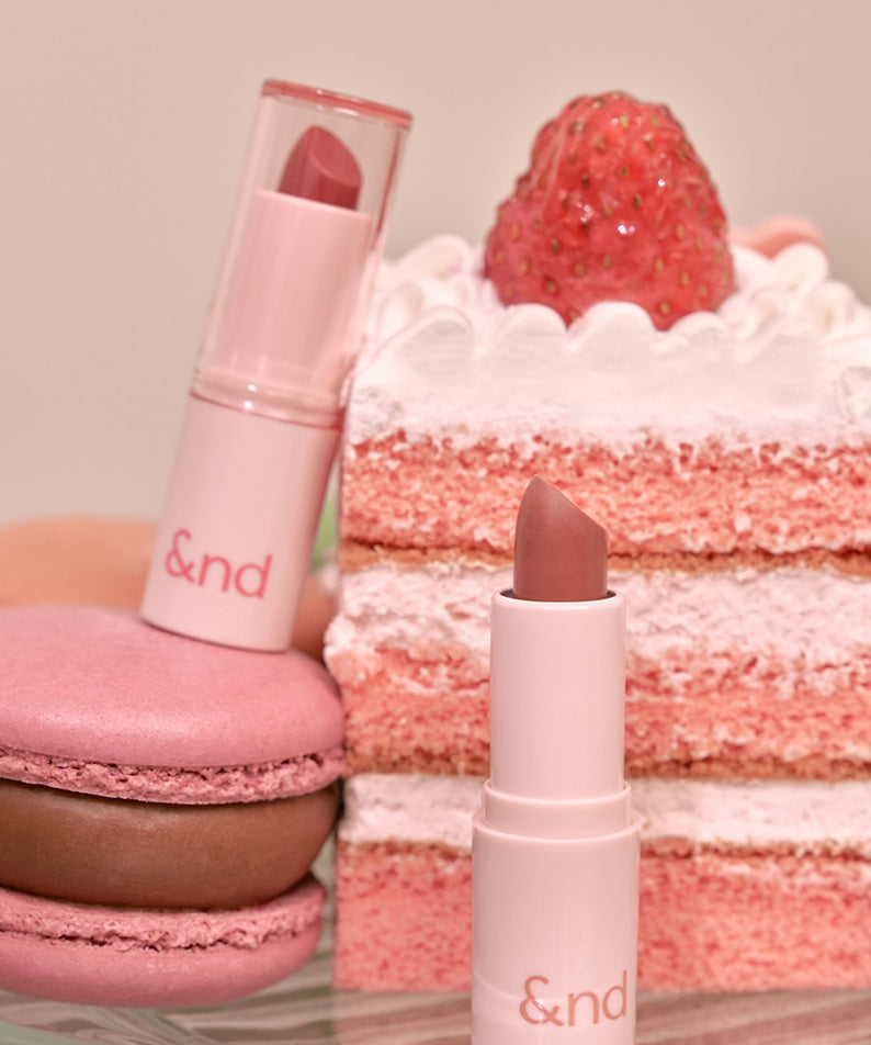 ROMAND  Glassy Bomb Balm en packaging, posé près de desserts fraise et macarons, contexte beauté studio